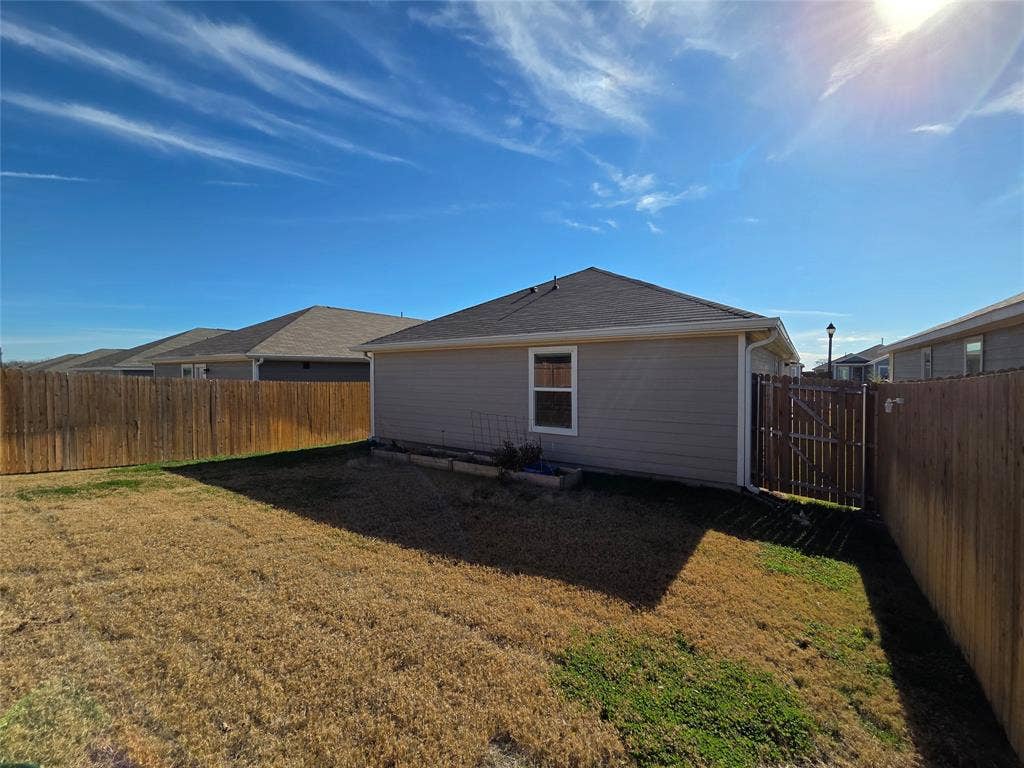 Expansive backyard featuring a wood privacy fence, a side gate, and a single window on the exterior wall