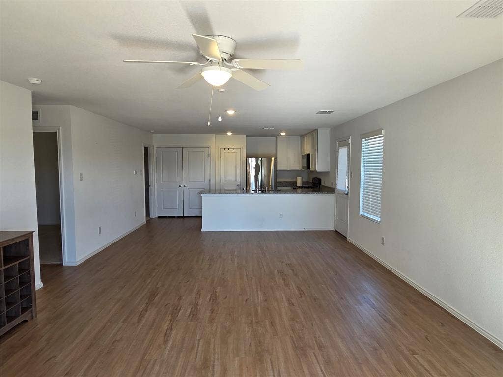 Open-concept layout featuring wood-finish flooring, white walls, and a ceiling fan with integrated lighting