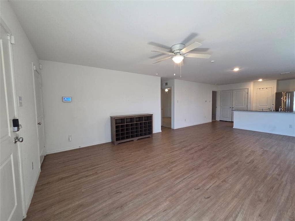 Spacious room featuring wood-finish flooring, white walls, and a ceiling fan with integrated lighting