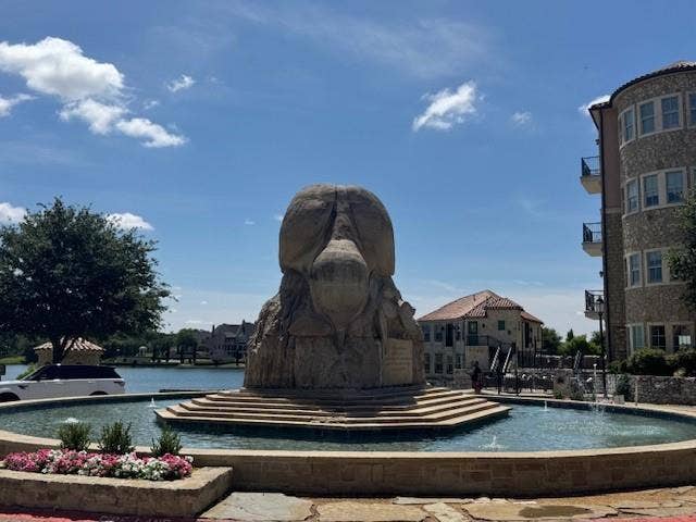 Stone facade building with multiple balconies, a structured water feature, and a prominent stone sculpture