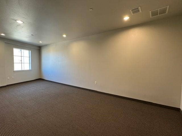 Spacious room featuring neutral wall tones, recessed lighting, a multi-pane window, and patterned carpet flooring