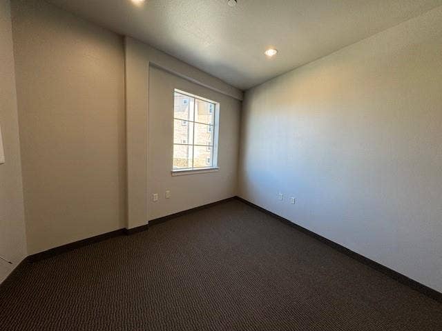 Recessed ceiling lighting, neutral-toned walls, a single window with white trim, and dark textured carpeting