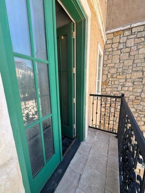 Balcony featuring tile flooring, decorative wrought iron railing, and a stone exterior wall