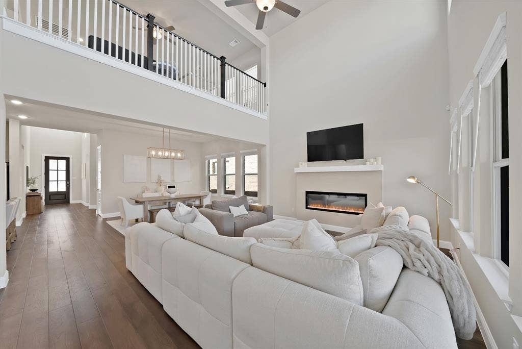 1837 Averi Lane, Farmers Branch, TX 75234 Two-story living area with high ceilings, wood-finish flooring, and an integrated electric fireplace below a mounted television