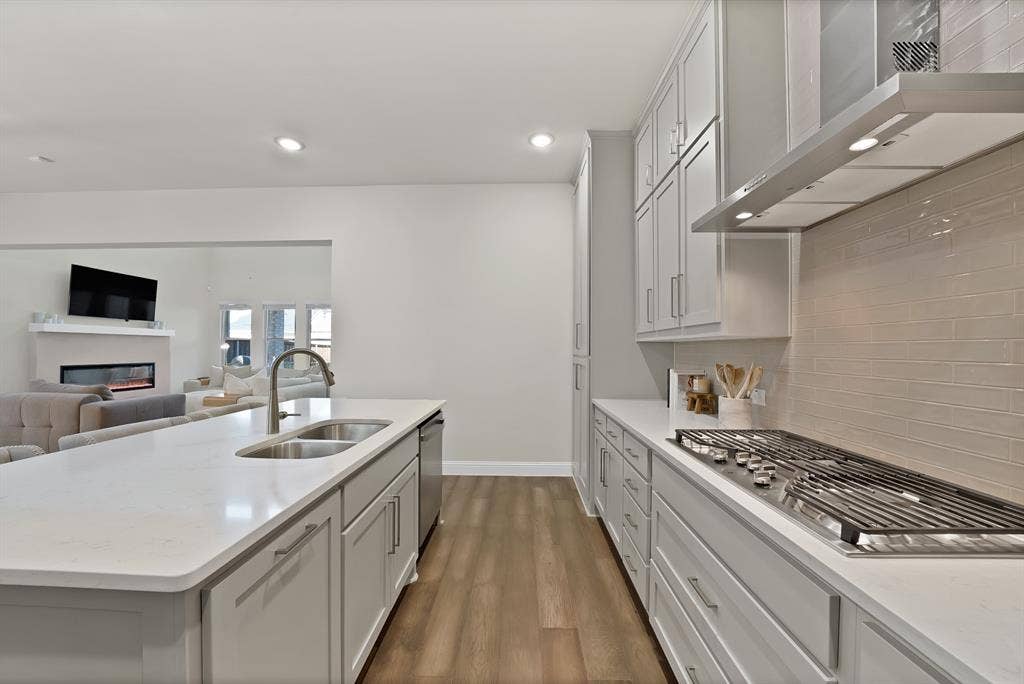 1837 Averi Lane, Farmers Branch, TX 75234 Modern kitchen featuring light gray cabinetry, stainless steel appliances, a white countertop island with a double basin sink, and wood-finish flooring