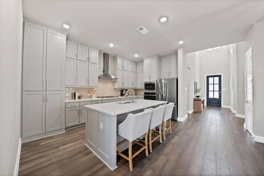 1837 Averi Lane, Farmers Branch, TX 75234 Kitchen featuring extensive light gray cabinetry, a large center island with integrated sink, stainless steel appliances, and wood-finish flooring
