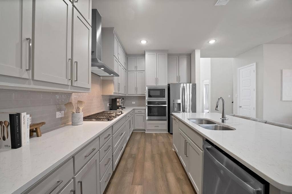 1837 Averi Lane, Farmers Branch, TX 75234 Modern kitchen featuring light gray cabinetry, stainless steel appliances, a center island with sink, white countertops, and wood-finish flooring