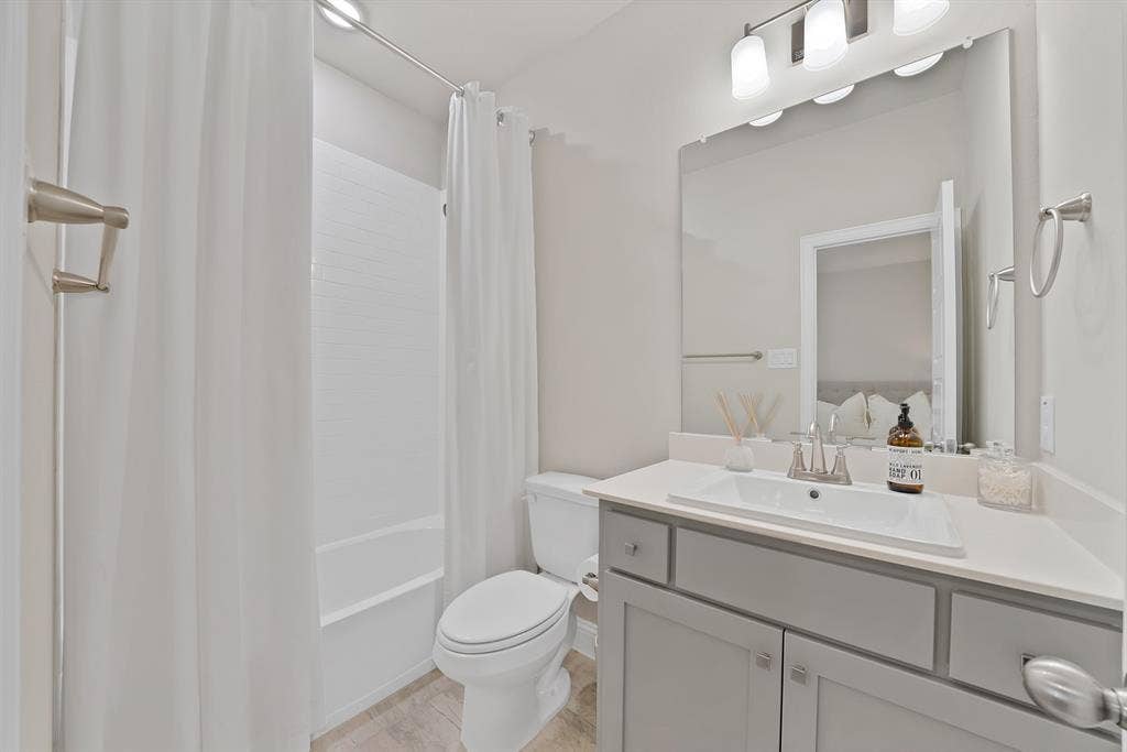 1837 Averi Lane, Farmers Branch, TX 75234 Bathroom featuring a white tub and shower combination, gray vanity with a single basin sink, light-colored countertop, and wall-mounted light fixture