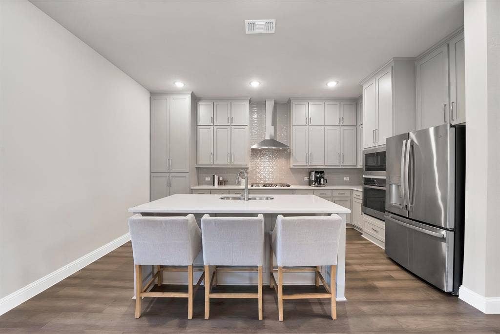 1837 Averi Lane, Farmers Branch, TX 75234 Contemporary kitchen featuring wood-finish flooring, light-colored cabinetry, a central island with an integrated sink, stainless steel appliances, and recessed lighting