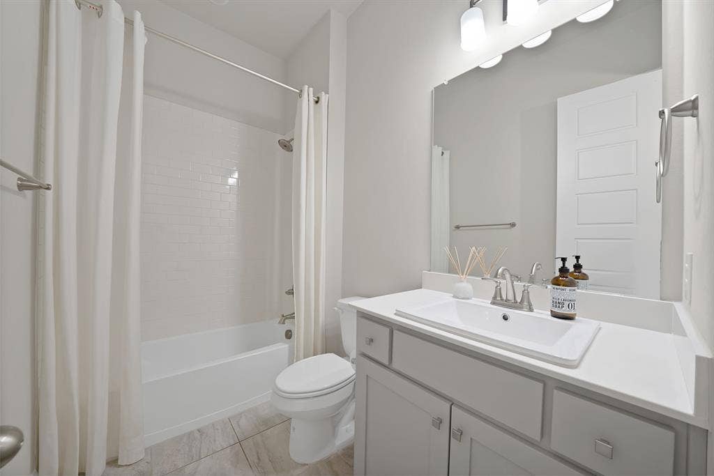 1837 Averi Lane, Farmers Branch, TX 75234 White subway tile bath surround, white tub, light gray vanity with rectangular integrated sink, neutral tile flooring, and brushed nickel hardware