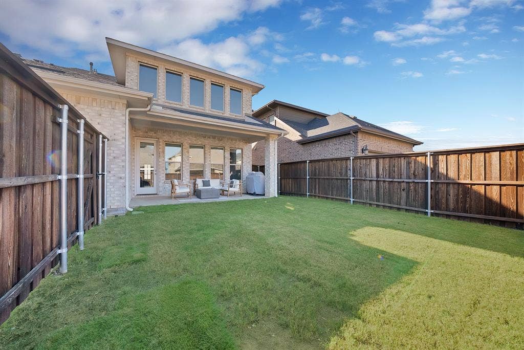 1837 Averi Lane, Farmers Branch, TX 75234 Expansive backyard with a covered patio, brick exterior, and a second-story dormer featuring a row of windows