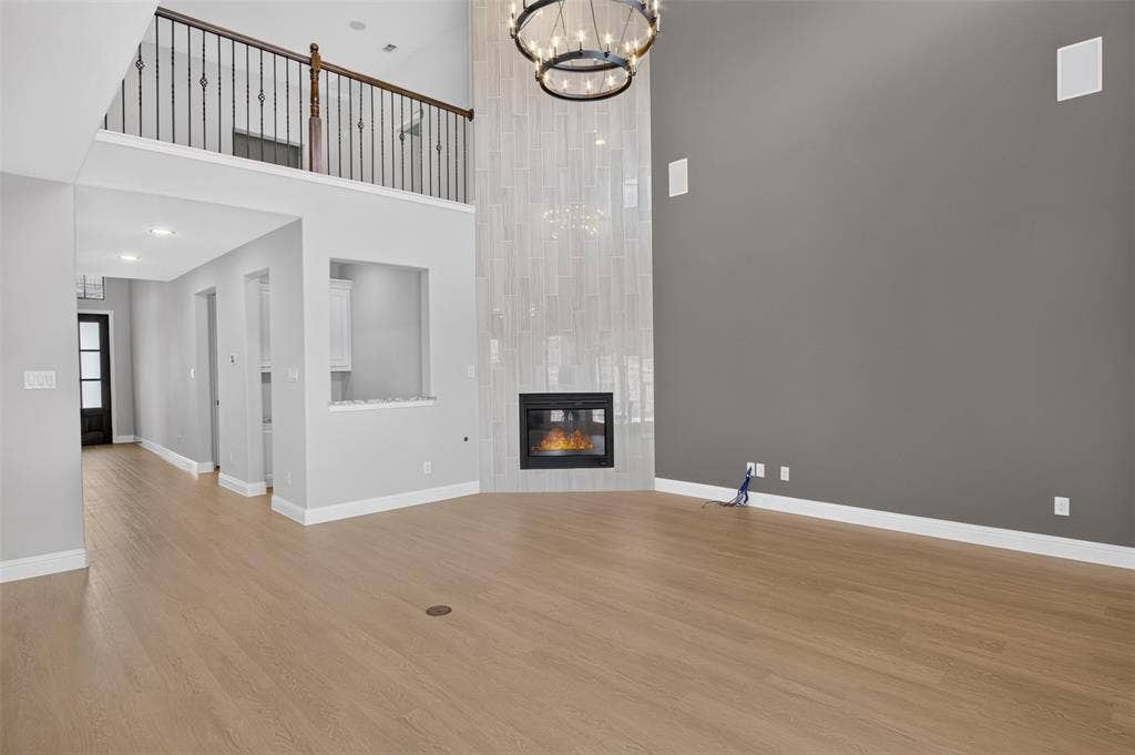 702 Callaway Drive, Allen, TX 75013 Two-story living area with wood-finish flooring, a contemporary fireplace with a tiled surround, a circular chandelier, and an upper-level balcony featuring a wrought iron railing