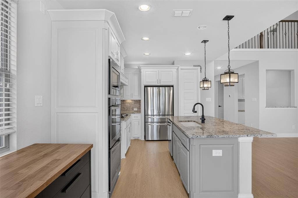 702 Callaway Drive, Allen, TX 75013 Modern kitchen featuring white cabinetry, stainless steel appliances, a center island with a speckled countertop, and recessed lighting