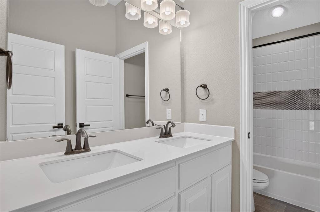 702 Callaway Drive, Allen, TX 75013 Double vanity with white cabinetry, integrated sinks, bronze-finish fixtures, and a large mirror