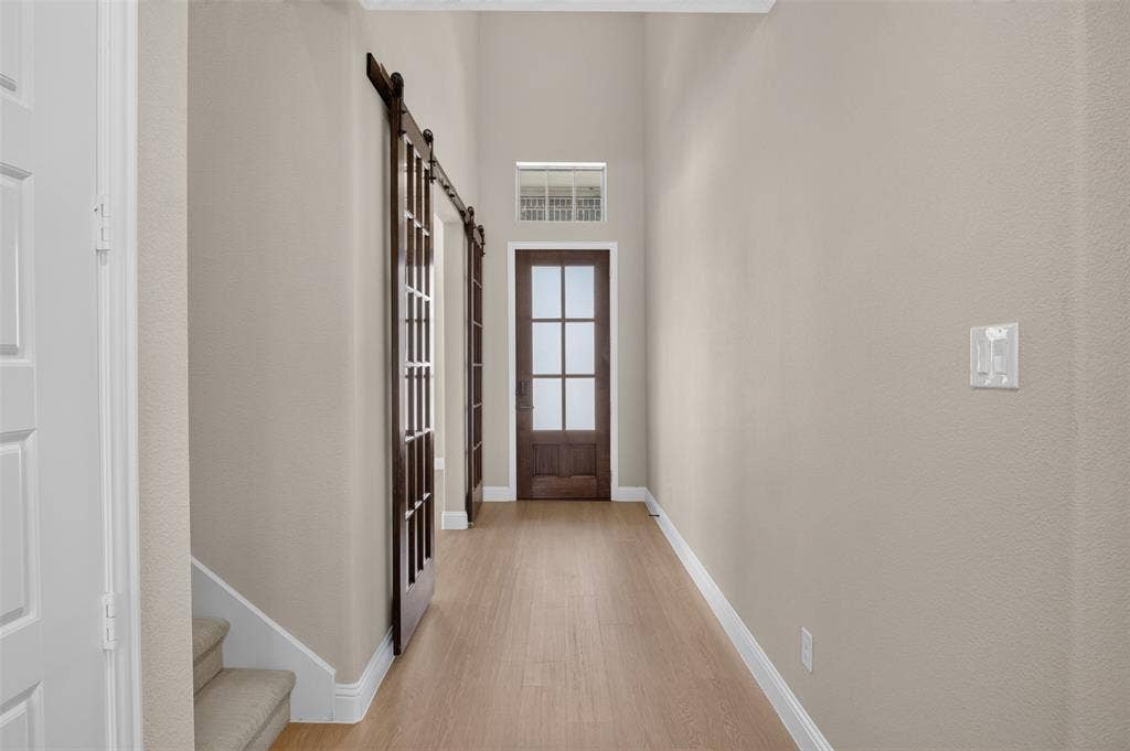 702 Callaway Drive, Allen, TX 75013 Hallway with wood-finish flooring, two dark wood barn doors, and a wood-frame door with frosted glass panels