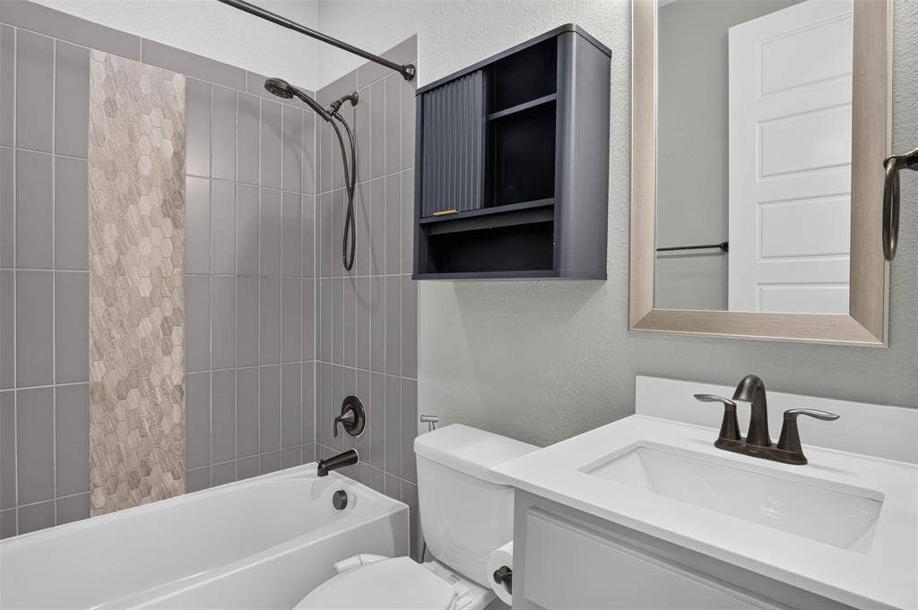 702 Callaway Drive, Allen, TX 75013 Bathroom featuring a shower-tub combination, vertical tile surround with an accent mosaic, white vanity with an integrated sink, and dark bronze fixtures