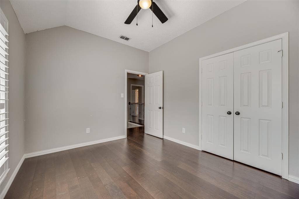 Vaulted ceiling with a ceiling fan, dark wood-finish flooring, and white bi-fold closet doors