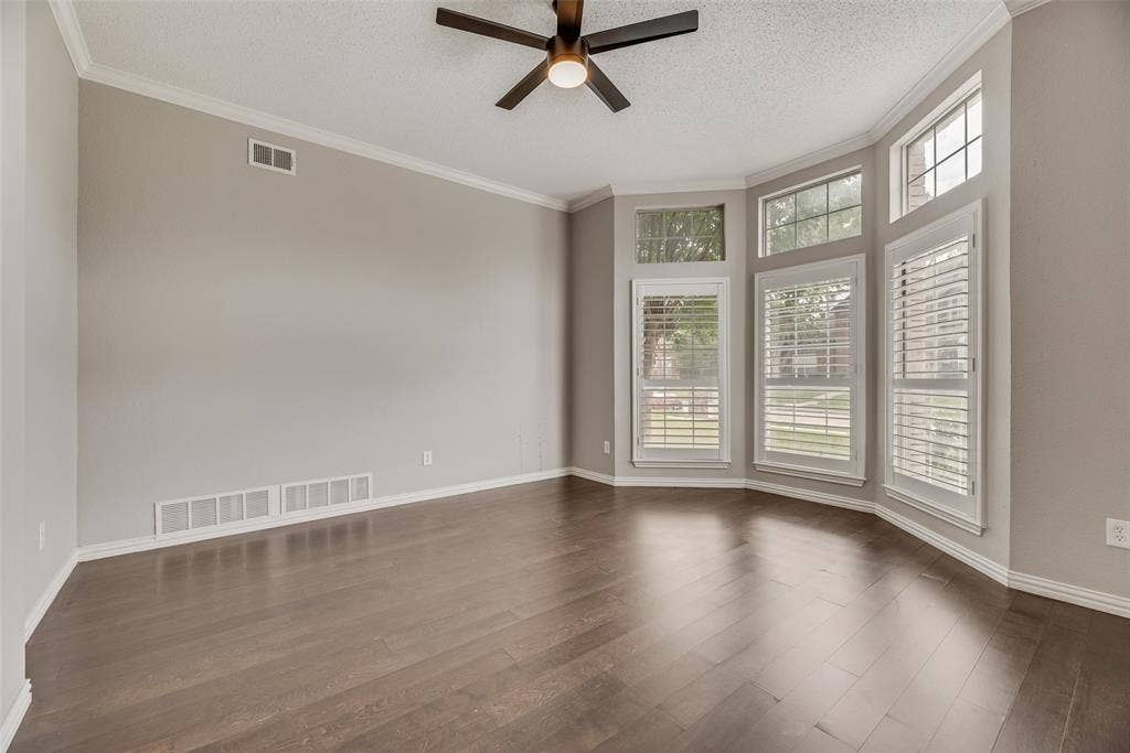 Wood-finish flooring, bay window with plantation shutters, ceiling fan, and crown molding
