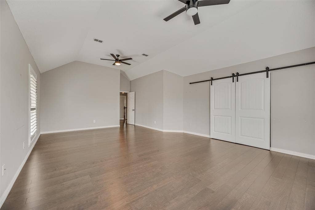 Vaulted ceiling with dual ceiling fans, wood-finish flooring, plantation shutters, and sliding barn doors