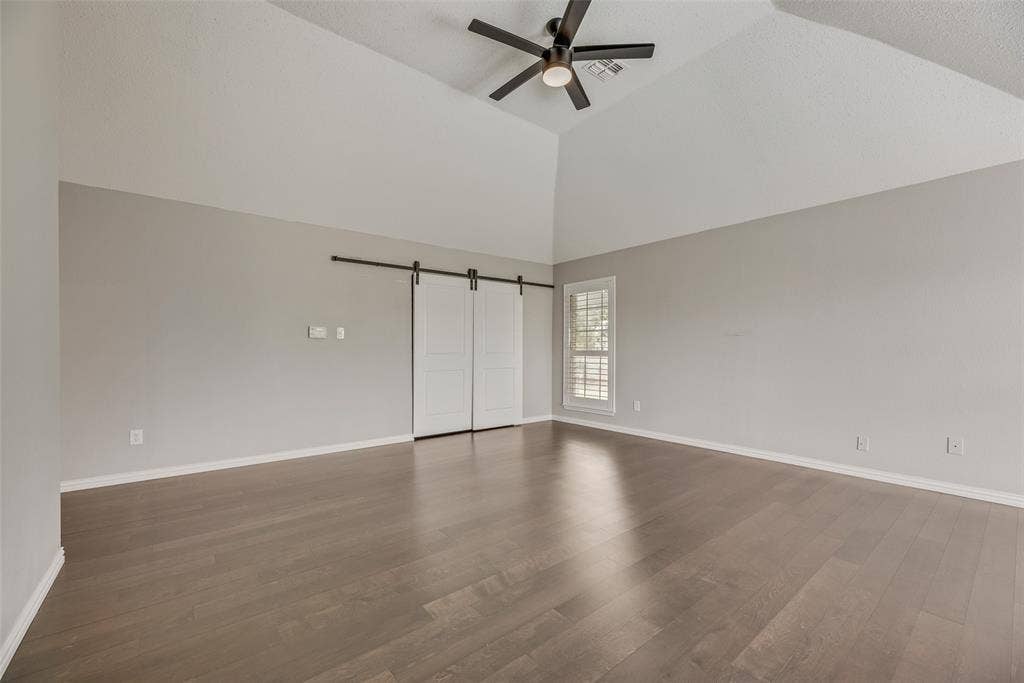 Vaulted ceiling, wood-finish flooring, ceiling fan, white plantation shutters, and barn doors