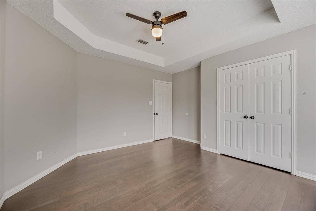 Wood-finish flooring, tray ceiling, ceiling fan with light, and paneled bifold closet doors