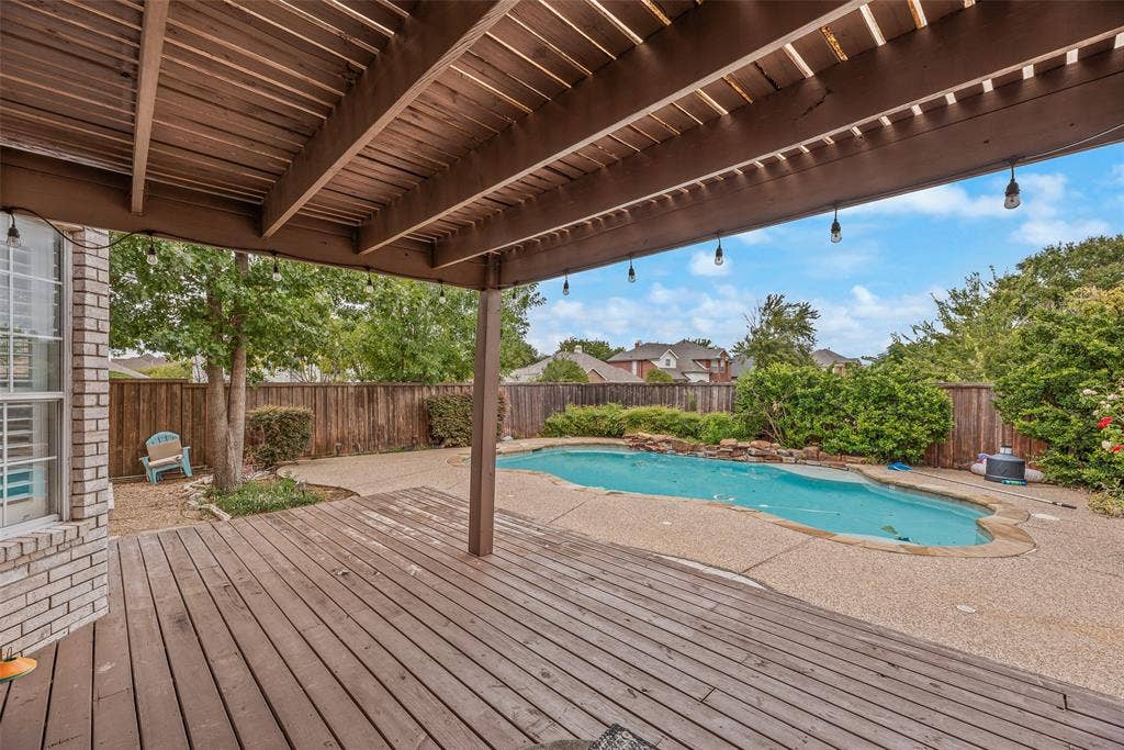 Expansive outdoor living area featuring a covered wood deck, a sparkling swimming pool, a rock waterfall, and privacy fencing