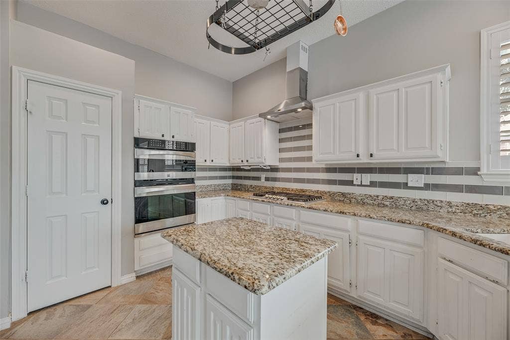Kitchen featuring white cabinetry, built-in double ovens, a central island with a granite countertop, and a tile backsplash