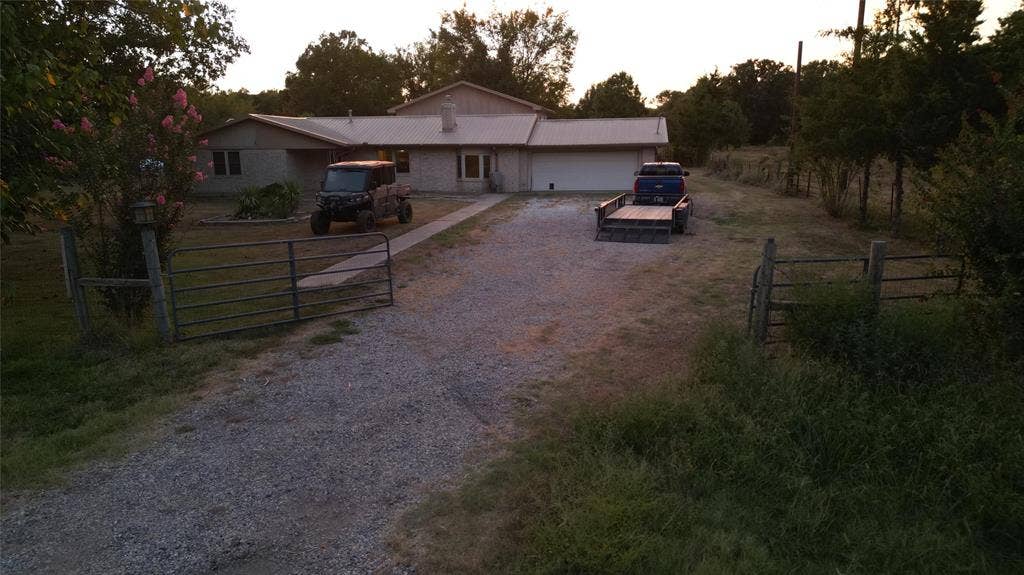 Single-story residence featuring a metal roof, attached two-car garage, gravel driveway, and gated entry