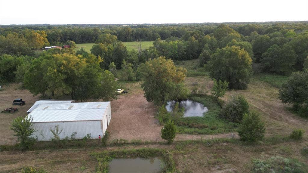 Aerial perspective featuring a metal-sided workshop, two ponds, and expansive acreage with mature trees