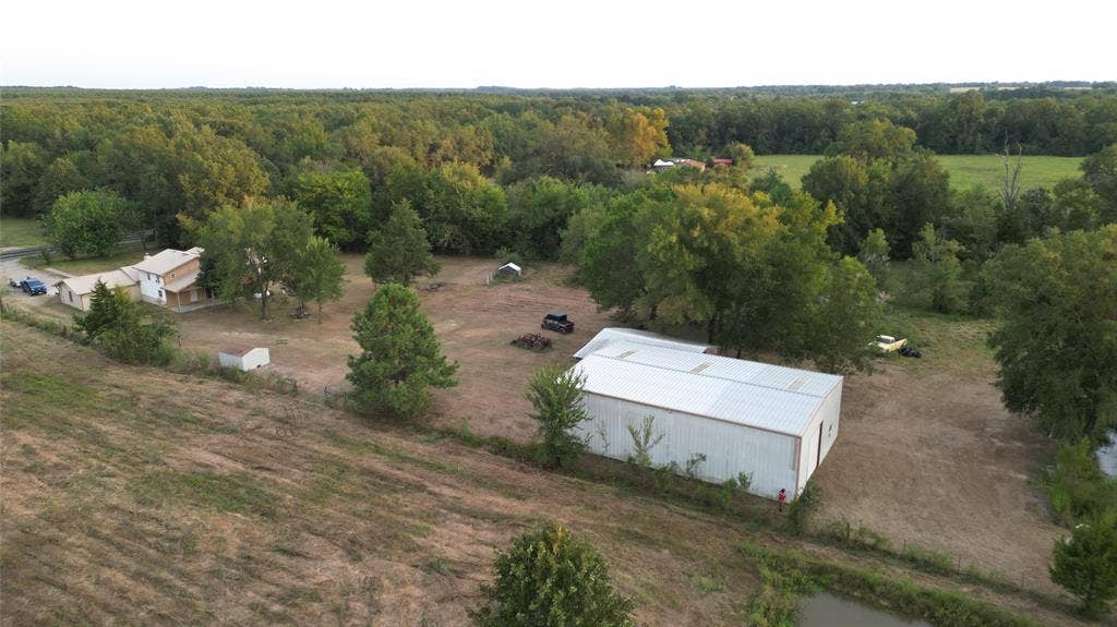 Extensive acreage featuring a detached metal-sided workshop, a multi-story residence, mature trees, and a pond