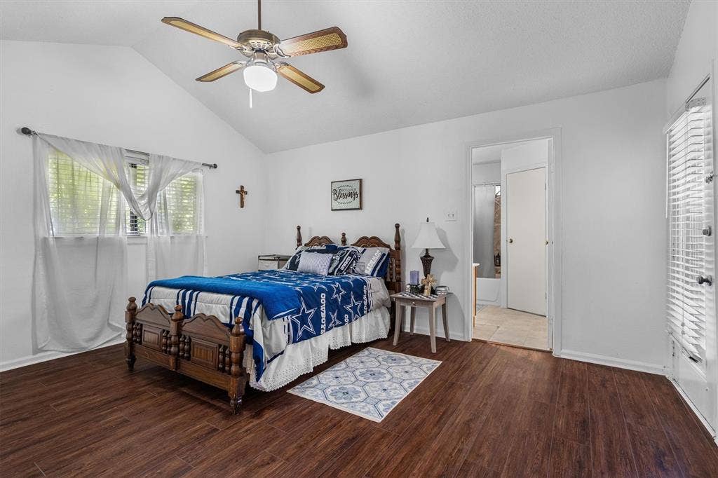 Vaulted ceiling with ceiling fan, wood-finish flooring, white walls, double window with blinds, and an interior door