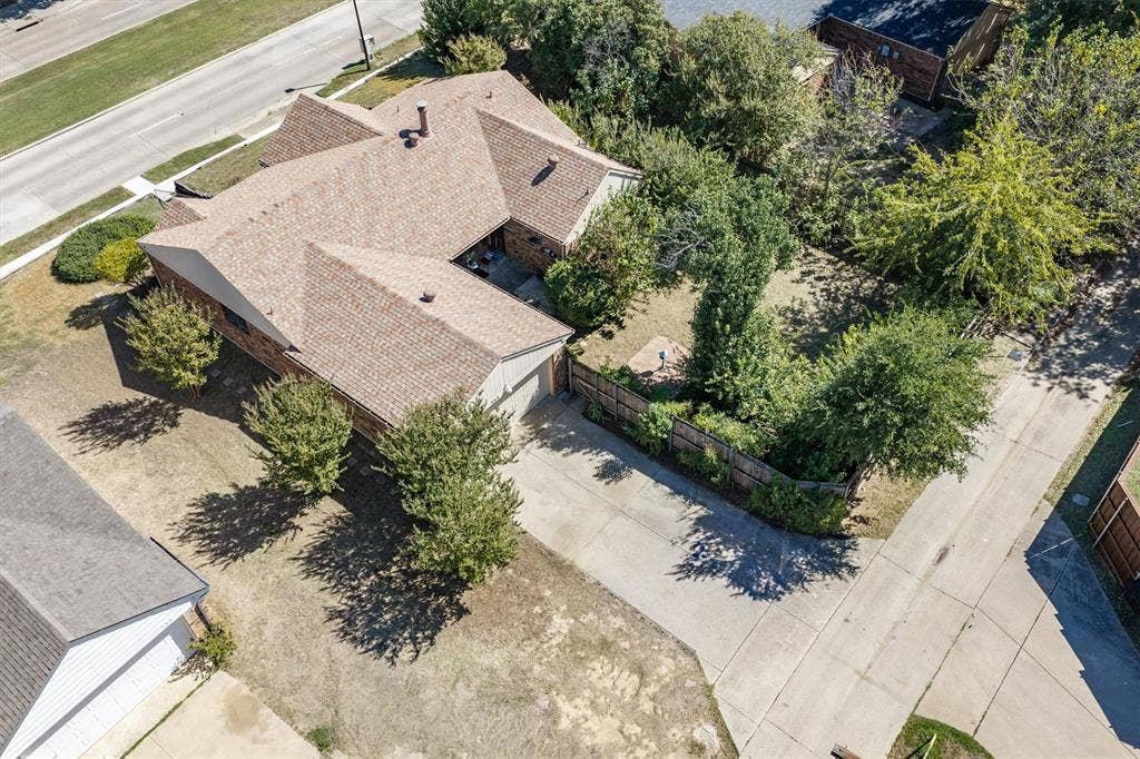 Brick exterior home with a shingle roof, attached garage, and mature landscaping
