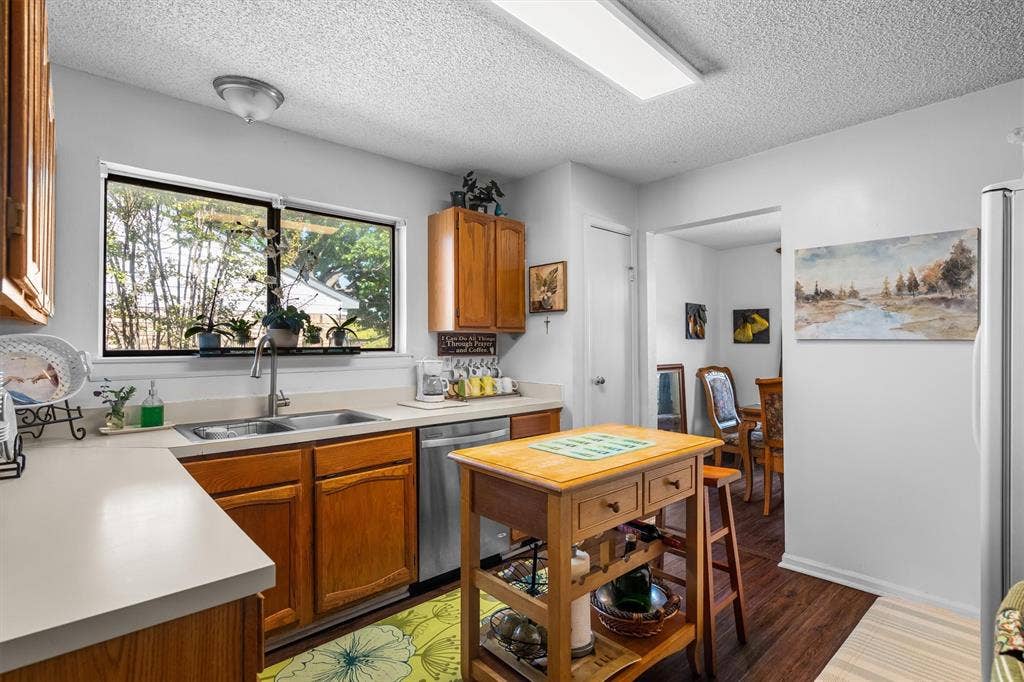 Kitchen featuring wood-finish cabinetry, light-toned countertops, a stainless steel sink, and wood-finish flooring