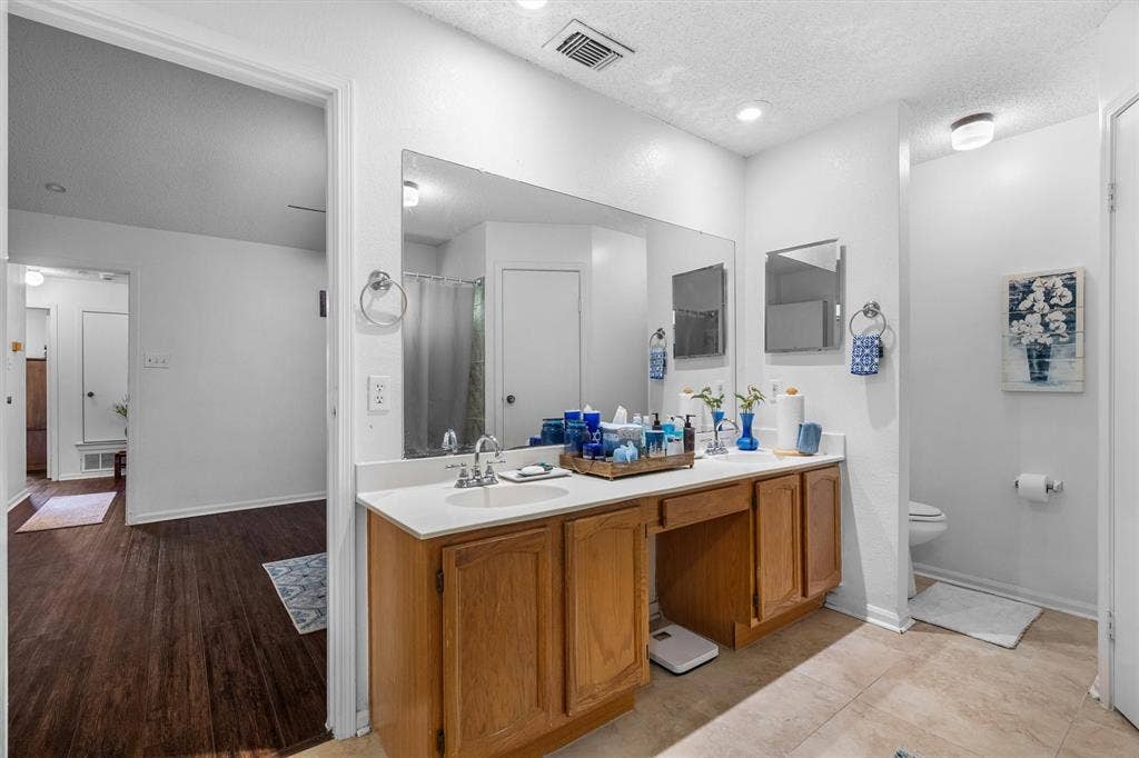 Double vanity with integrated sinks, wood cabinetry, expansive mirror, and overhead recessed lighting