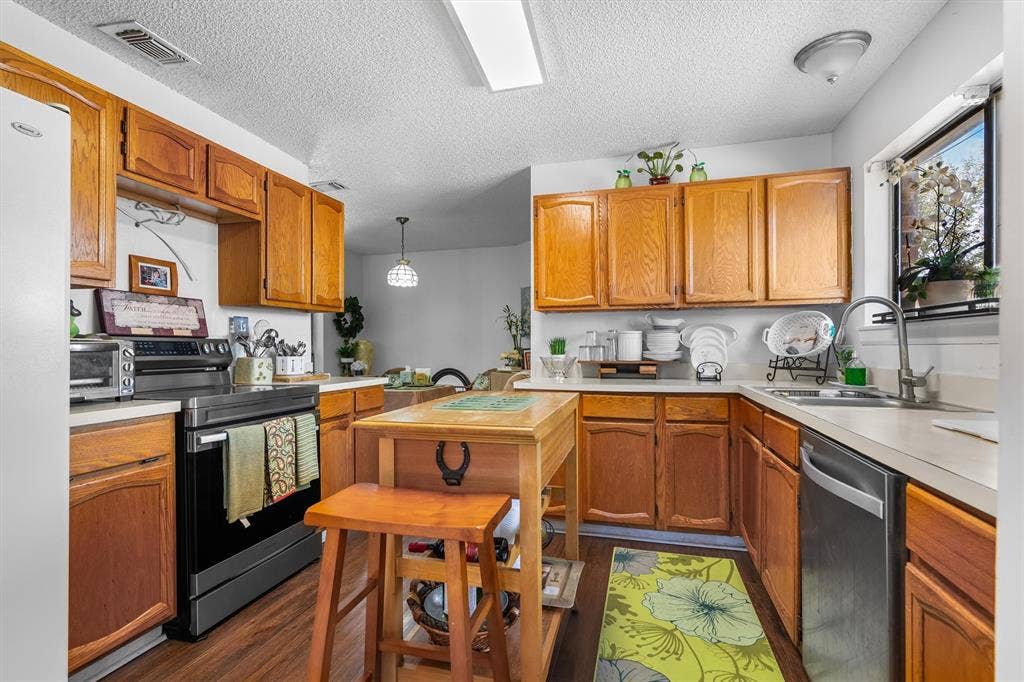 Wood-finish flooring, wood cabinetry, stainless steel dishwasher, stainless steel range, and a window with a built-in shelf