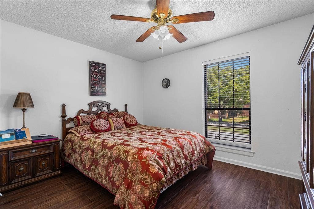 Wood-finish flooring, ceiling fan with light fixture, window with blinds, and white walls