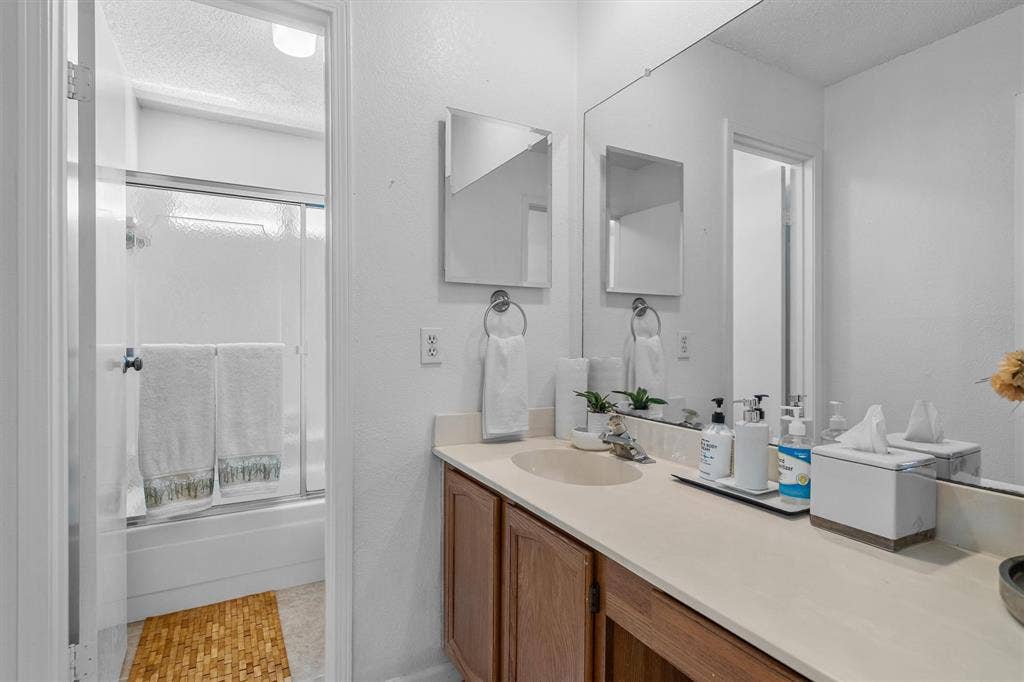 Full-width mirror, wood-finish vanity with integrated sink, and shower-tub combination with sliding glass doors