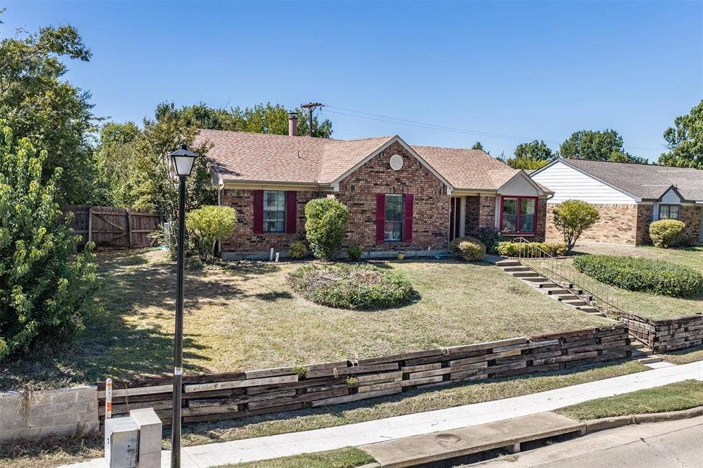 Brick exterior with red shutters, stepped entry with handrails, and a terraced front yard featuring a wood retaining wall