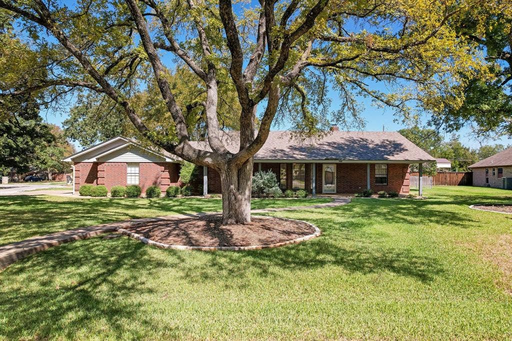 5203 Thunderbird Trail, De Cordova, TX 76049 Brick exterior with a covered front porch, large mature tree, established landscaping, and a manicured lawn