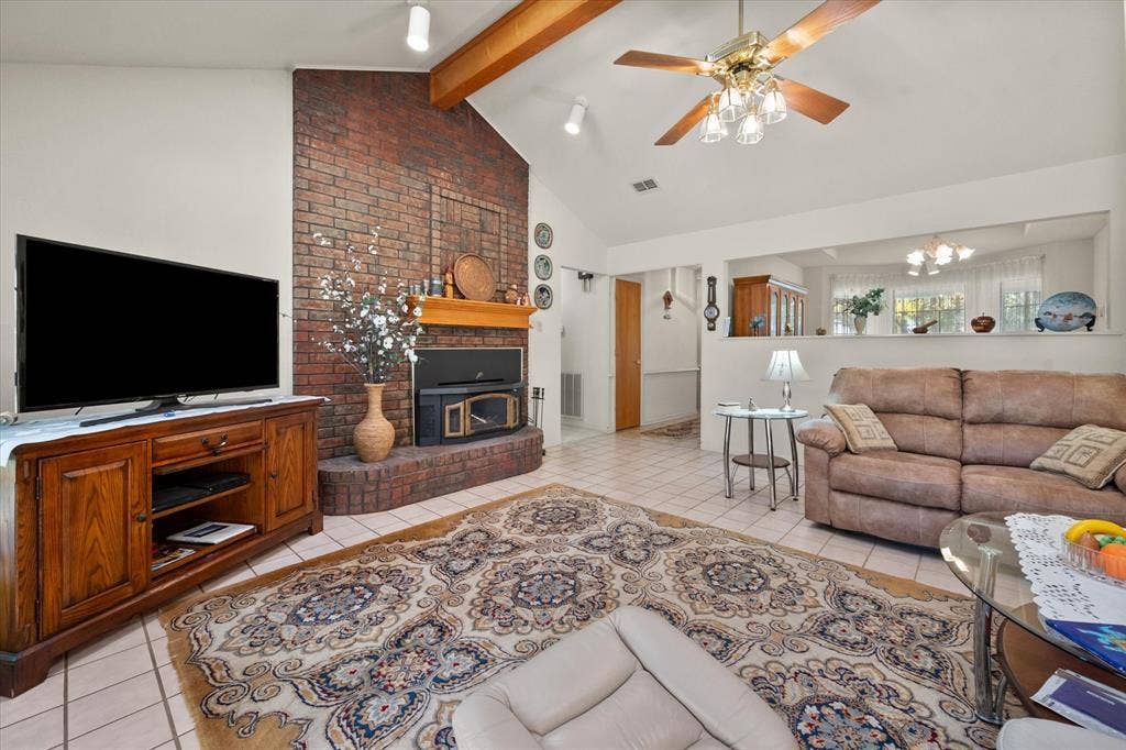 5203 Thunderbird Trail, De Cordova, TX 76049 Vaulted ceiling with exposed wood beams, brick fireplace, tile flooring, and a ceiling fan with integrated lighting