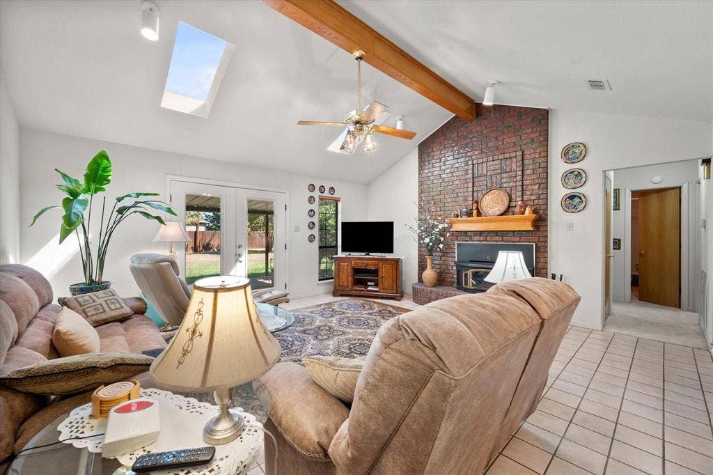 5203 Thunderbird Trail, De Cordova, TX 76049 Vaulted ceiling with exposed wood beams, skylight, brick fireplace with wood mantel, ceiling fan with light fixture, and tile flooring