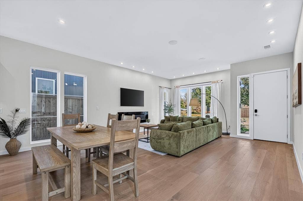 Spacious open-concept living area featuring wood-finish flooring, recessed lighting, expansive windows, and a built-in fireplace