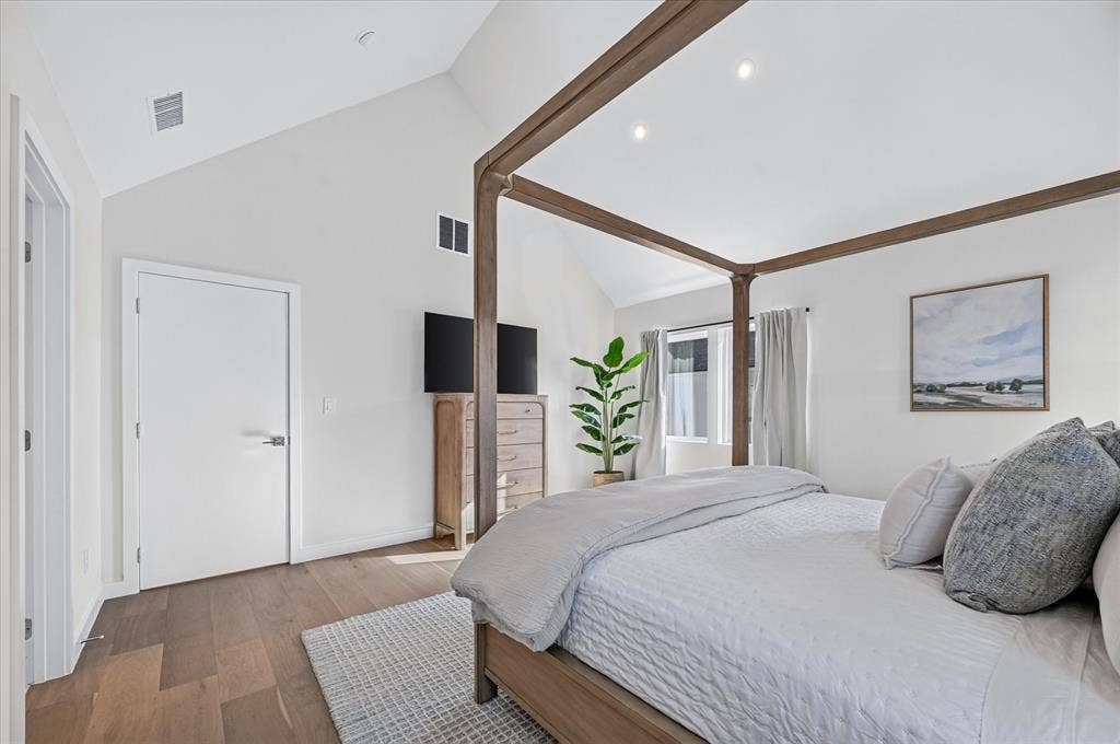 Vaulted ceiling with recessed lighting, wood-finish flooring, white flat-panel doors, and a window with natural light