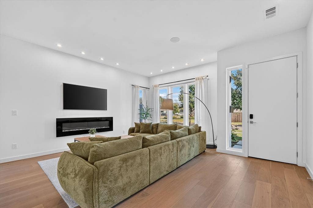 Recessed lighting, wood-finish flooring, large windows, wall-mounted electric fireplace, and a side-light entry door