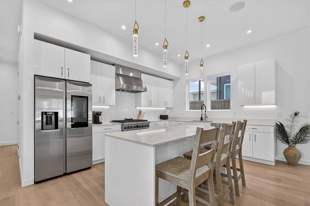 Gourmet kitchen with stainless steel appliances, a center island with seating, pendant lighting, white cabinetry, and wood-finish flooring