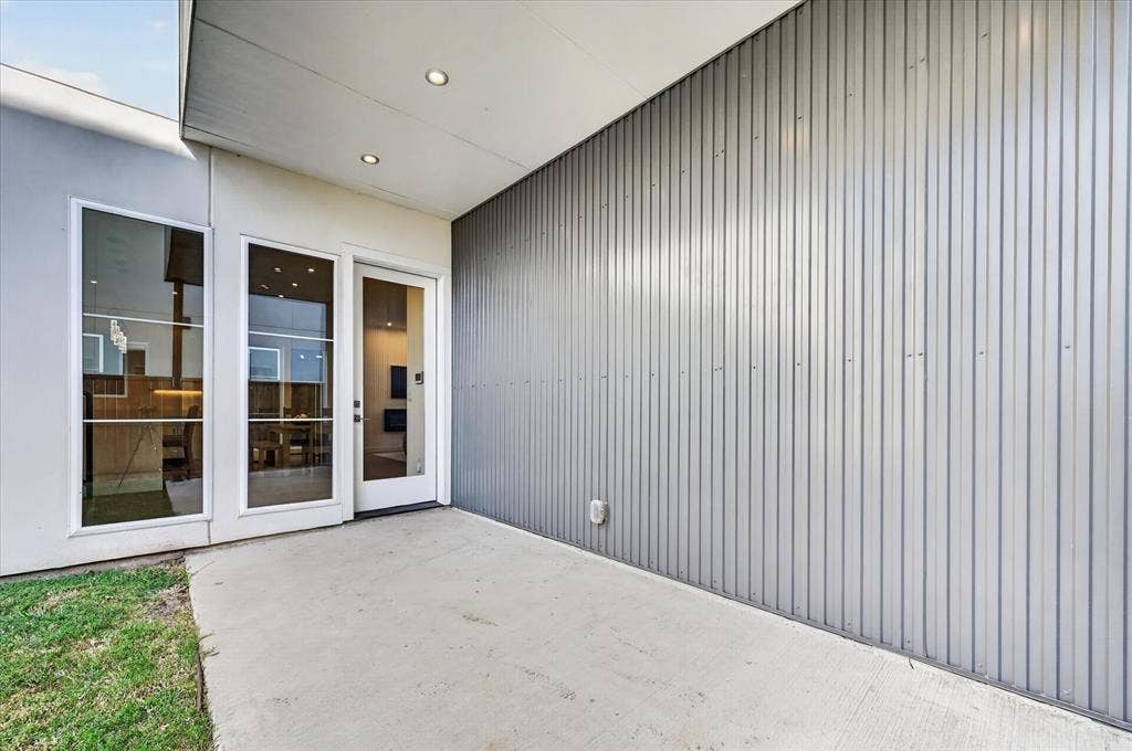 Concrete patio with a corrugated metal exterior wall, recessed lighting, and a glass-paneled entry door