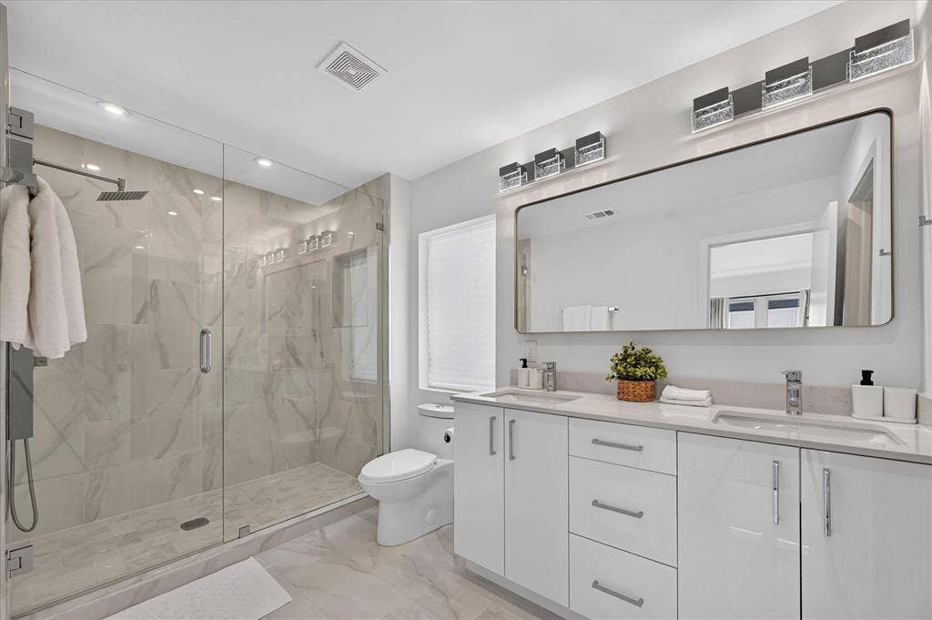 Dual vanity with integrated sinks and white cabinetry, expansive frameless mirror, and overhead decorative lighting