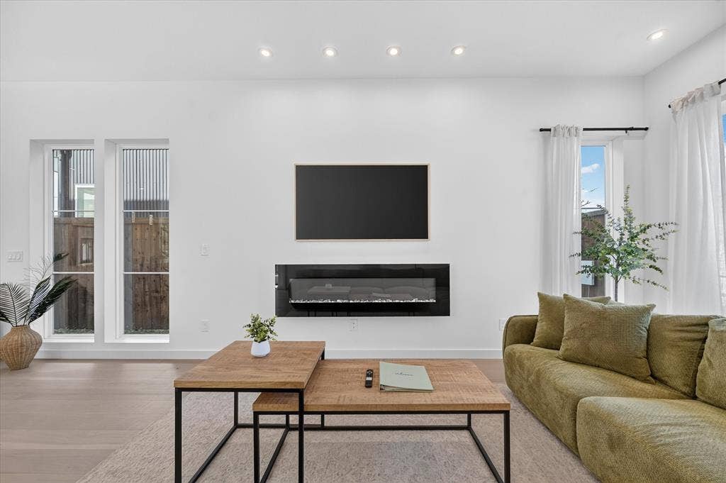 Recessed ceiling lighting illuminates a white wall with a mounted linear electric fireplace