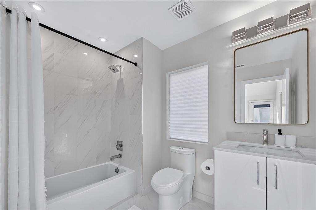 Bathtub and shower combination with white tile surround, vanity with an integrated sink, rectangular mirror, and ceiling-mounted lighting