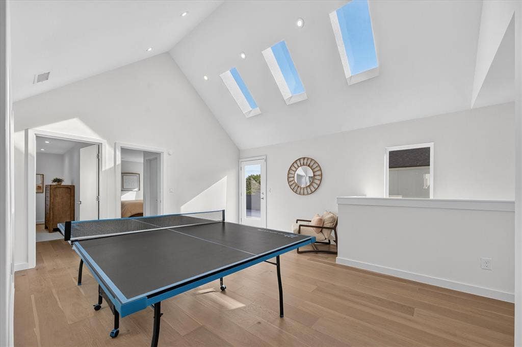 Vaulted ceiling with multiple skylights, recessed lighting, wood-finish flooring, and a white half-wall partition